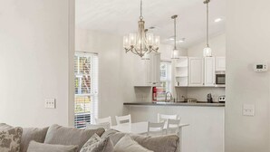 A modern kitchen with white cabinets, a dining area with a white table and chairs, and a chandelier. - Oceanside Village - Beautiful 3BR 2BA - Golf Cart Included! (Surfside Beach)