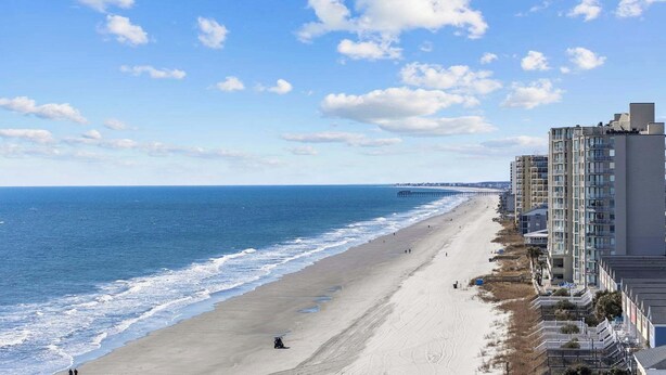 A beach with a pier in the distance, adjacent to a row of high-rise buildings. - Oceanside Village - Beautiful 3BR 2BA - Golf Cart Included! (Surfside Beach)