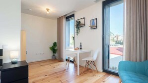 Ein modernes Wohnzimmer mit Holzboden, einem weißen Tisch mit Stühlen, einem blauen Sofa und einem großen Fenster mit Vorhängen.