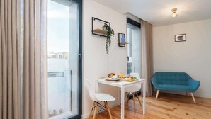 Ein modernes Wohnzimmer mit Esstisch für zwei Personen, einem blauen Sofa und einer Glastür, die auf einen Balkon führt.