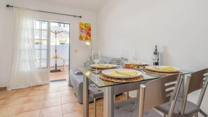 Een eetruimte met een glazen tafel, gestoffeerde grijze stoelen en uitzicht buiten door een glazen deur.