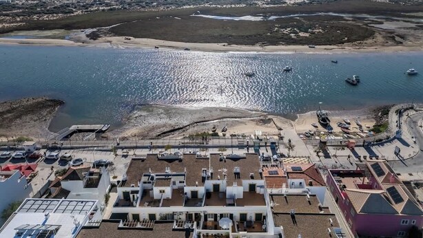 Luchtbeeld van een kustgebied met een jachthaven, gebouwen met platte daken en een strand.
