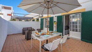 Een terras met een tafel voor twee personen, een barbecue en een grote parasol.