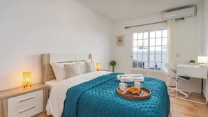 Een moderne hotelkamer met een bed, nachtkastje, bureau en een raam met uitzicht.