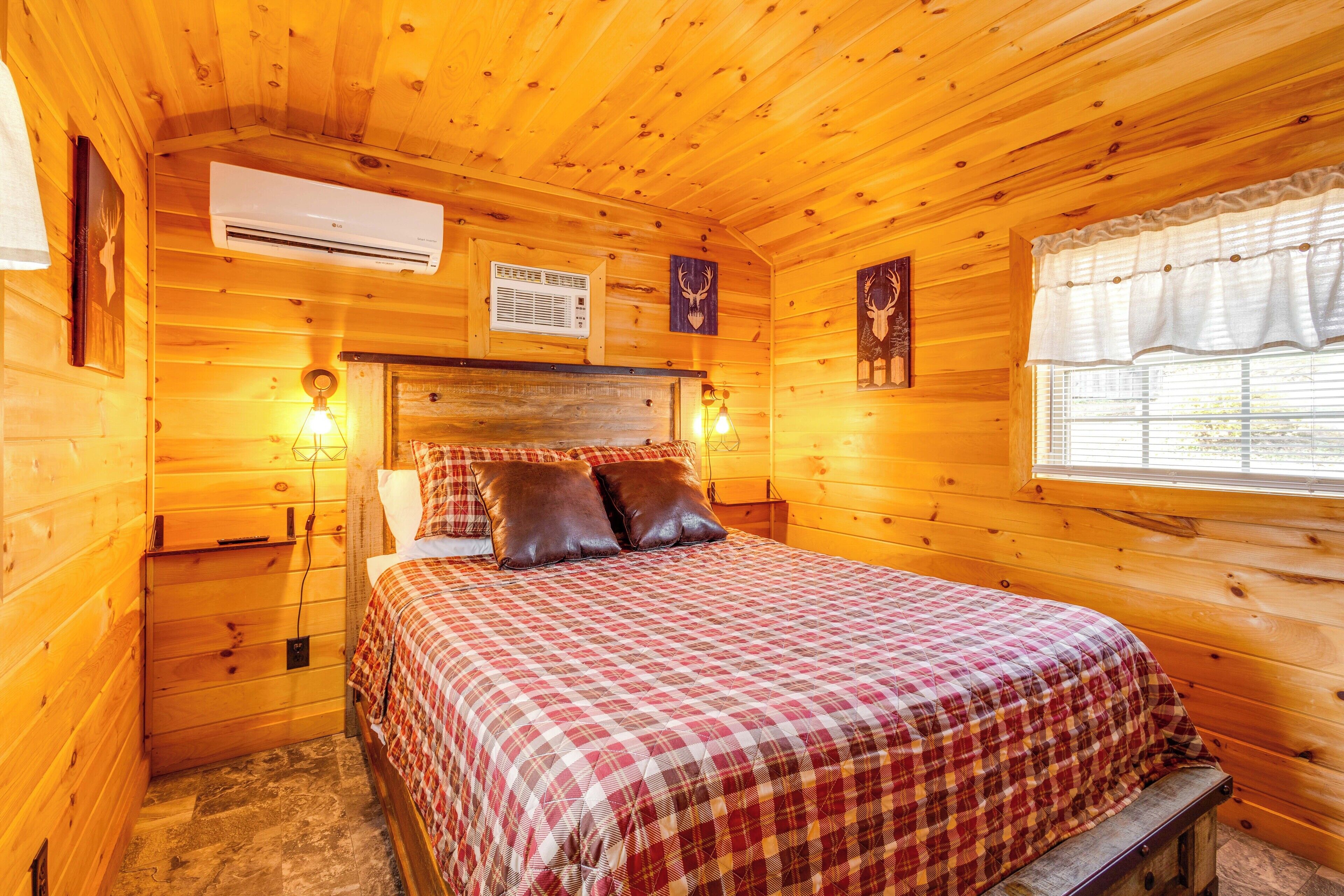 Un dormitori de cabana de fusta amb un llit, una taula de nit, aire condicionat i una finestra amb cortines.