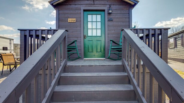 A wooden cabin with a green door, a staircase with a railing, and two rocking chairs.