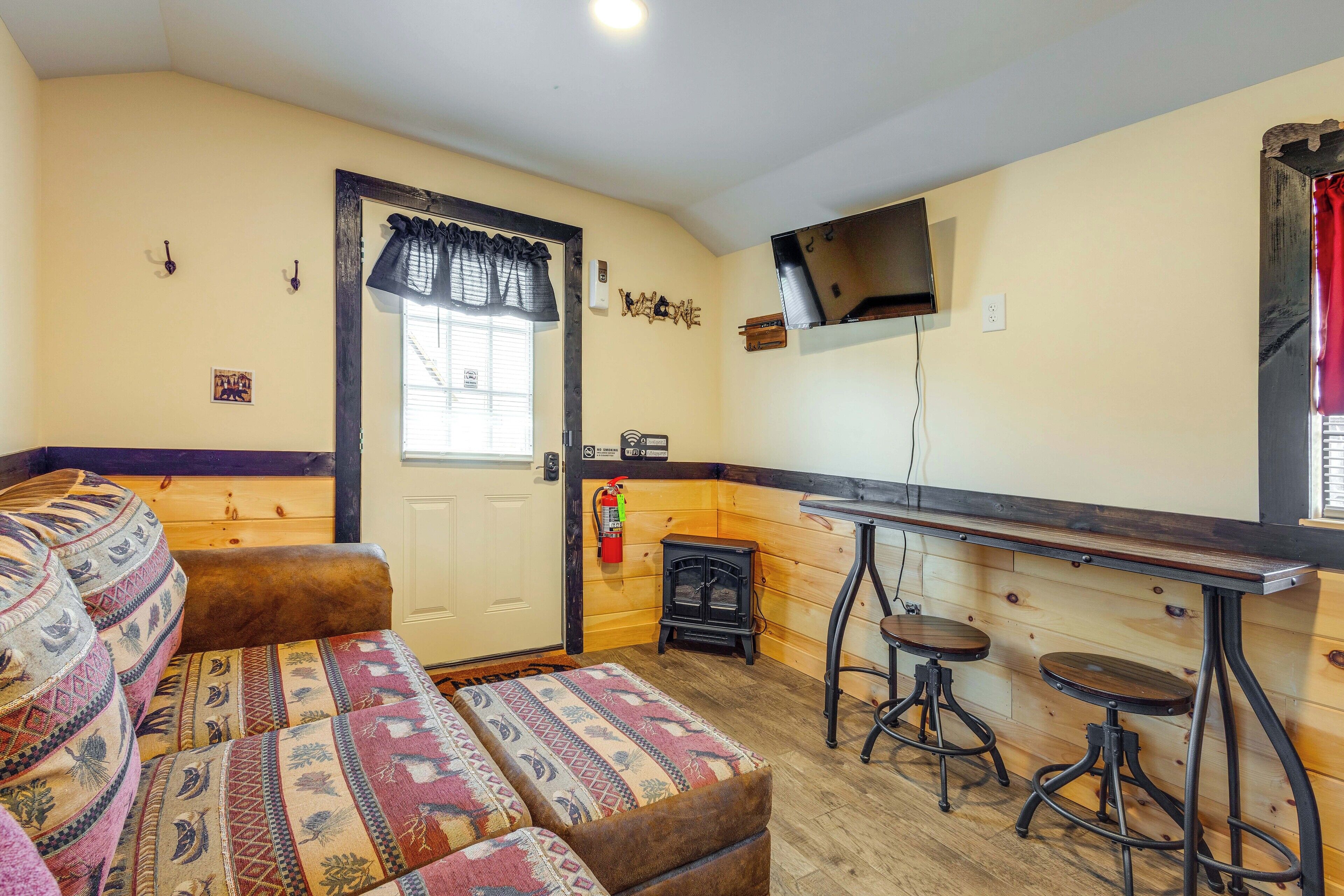 Una habitación acogedora con sofá, una pequeña mesa con taburetes, televisión y chimenea.