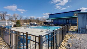 A rectangular swimming pool surrounded by a metal fence, with lounge chairs and a covered area nearby.