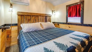 A bedroom with a wooden headboard, a bed with a blue and white quilt, bedside lamps, and a window with red curtains.