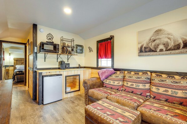 A compact living space with a kitchenette, a sofa with patterned cushions, and a bear-themed wall hanging.
