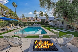 A swimming pool with lounge chairs, a fire pit, and a well-maintained lawn.