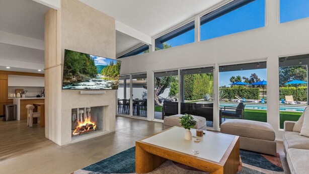 Ein modernes Wohnzimmer mit Kamin, Flachbildfernseher und Blick auf einen Pool und Sitzgelegenheiten im Freien.