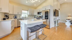 Cocina moderna con armarios blancos, una isla central con taburetes altos, electrodomésticos de acero inoxidable y una lámpara colgante.