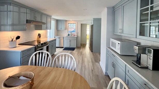 A modern kitchen with light blue cabinets, stainless steel appliances, and a wooden dining table. - The perfect cozy Chatham getaway awaits you! (Chatham)