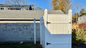 A white outdoor storage shed with a door and a small step leading up to it. - The perfect cozy Chatham getaway awaits you! (Chatham)