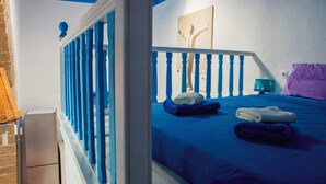 Une chambre avec une couvre-lit bleue, un mur blanc orné d’un tableau et une balustrade bleue.