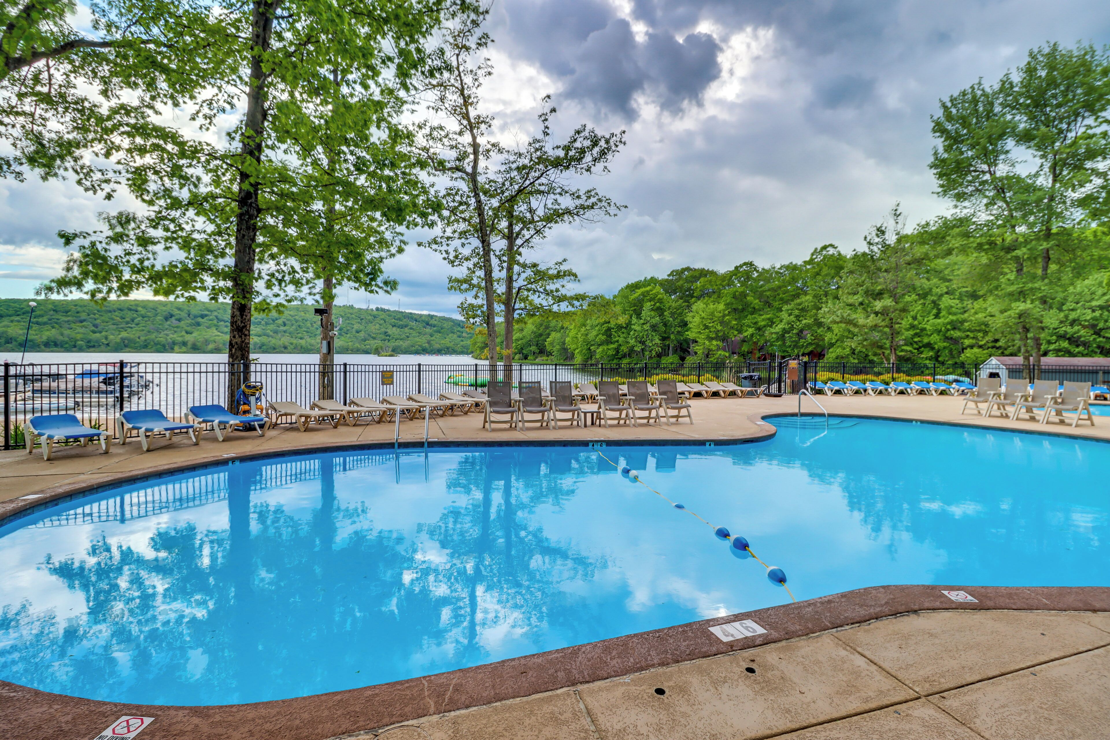 A swimming pool with lounge chairs and a view of a lake and forest.