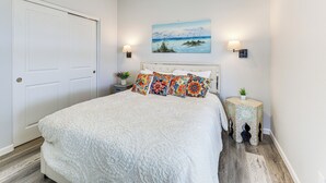 Quarto com uma cama grande, duas luminárias na parede, um quadro e uma pequena mesa com uma planta.