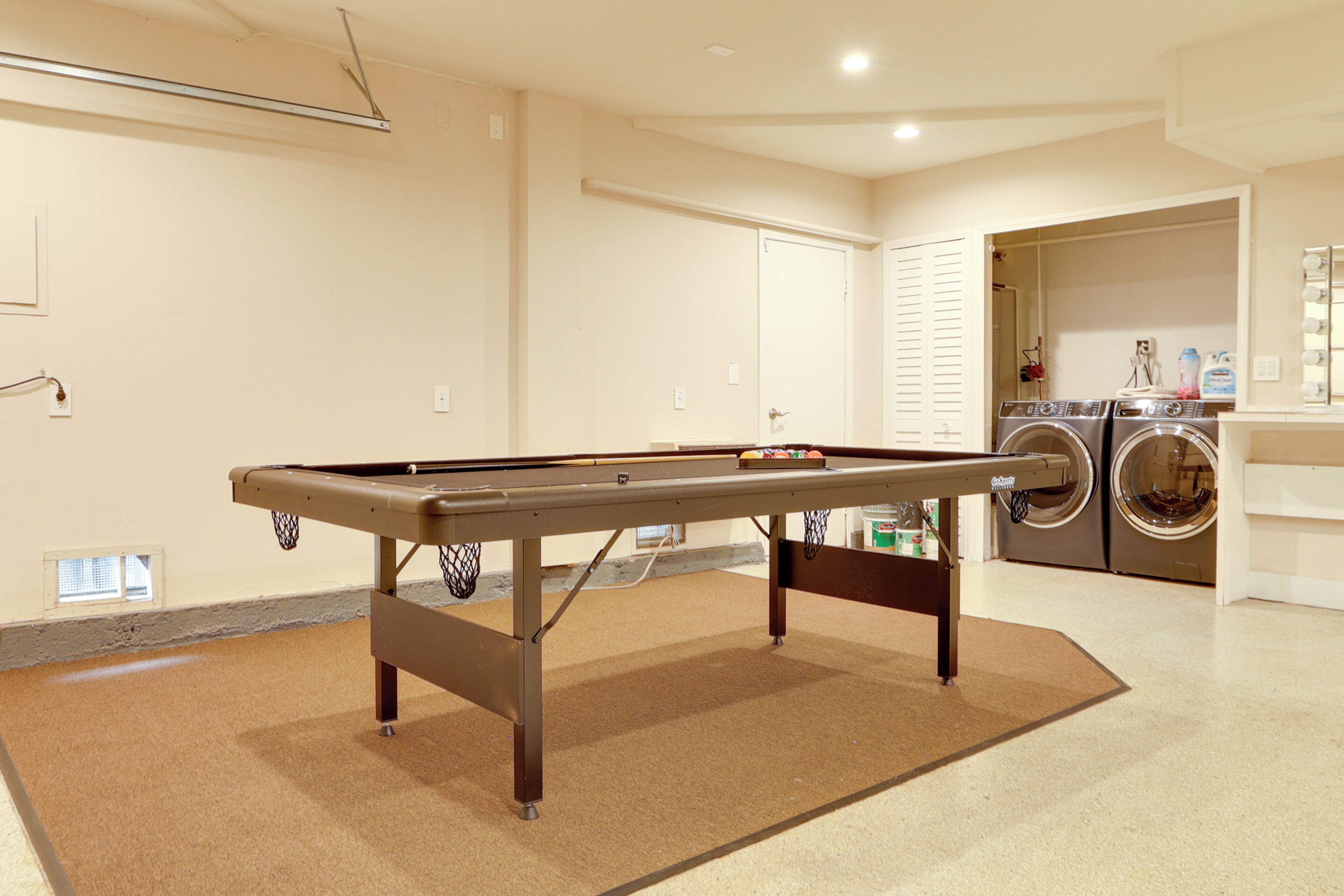 A pool table in a room with a laundry area and a door leading to another room.