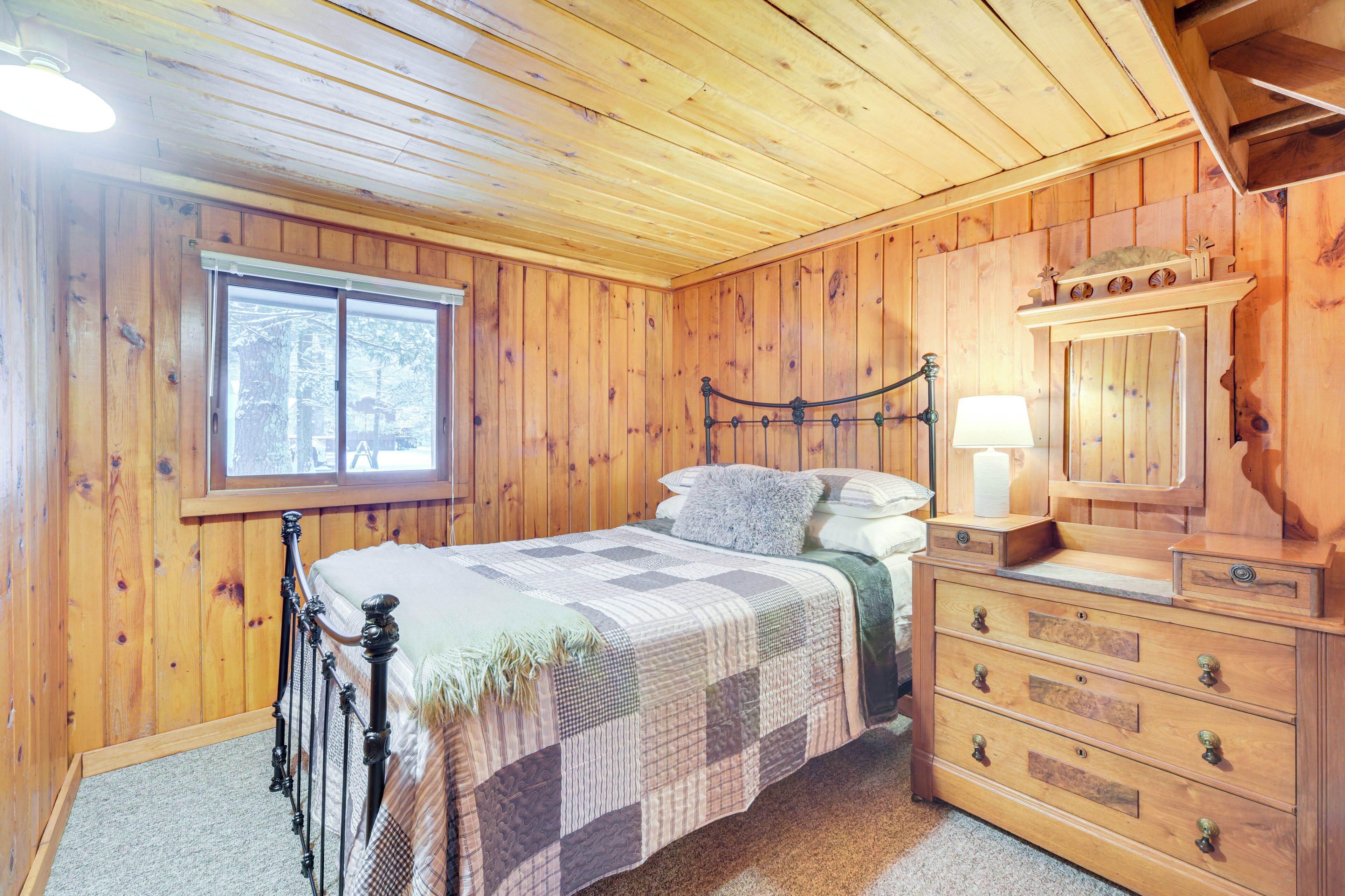 Een slaapkamer met houten lambrisering, een bed, een kast en een raam.