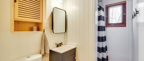 Ein Badezimmer mit Toilette, Waschbecken, Spiegel, Holzschrank und Fenster mit Holzrahmen.