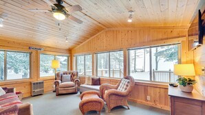 A cozy cabin interior with wooden walls, large windows, a fireplace, and comfortable seating. - Charming Cabin on Grindstone Lake (Hayward)