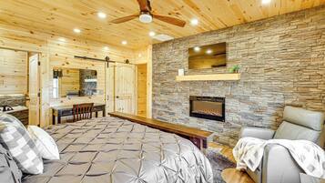 A bedroom with a large bed, a fireplace, a stone wall, and a ceiling fan.