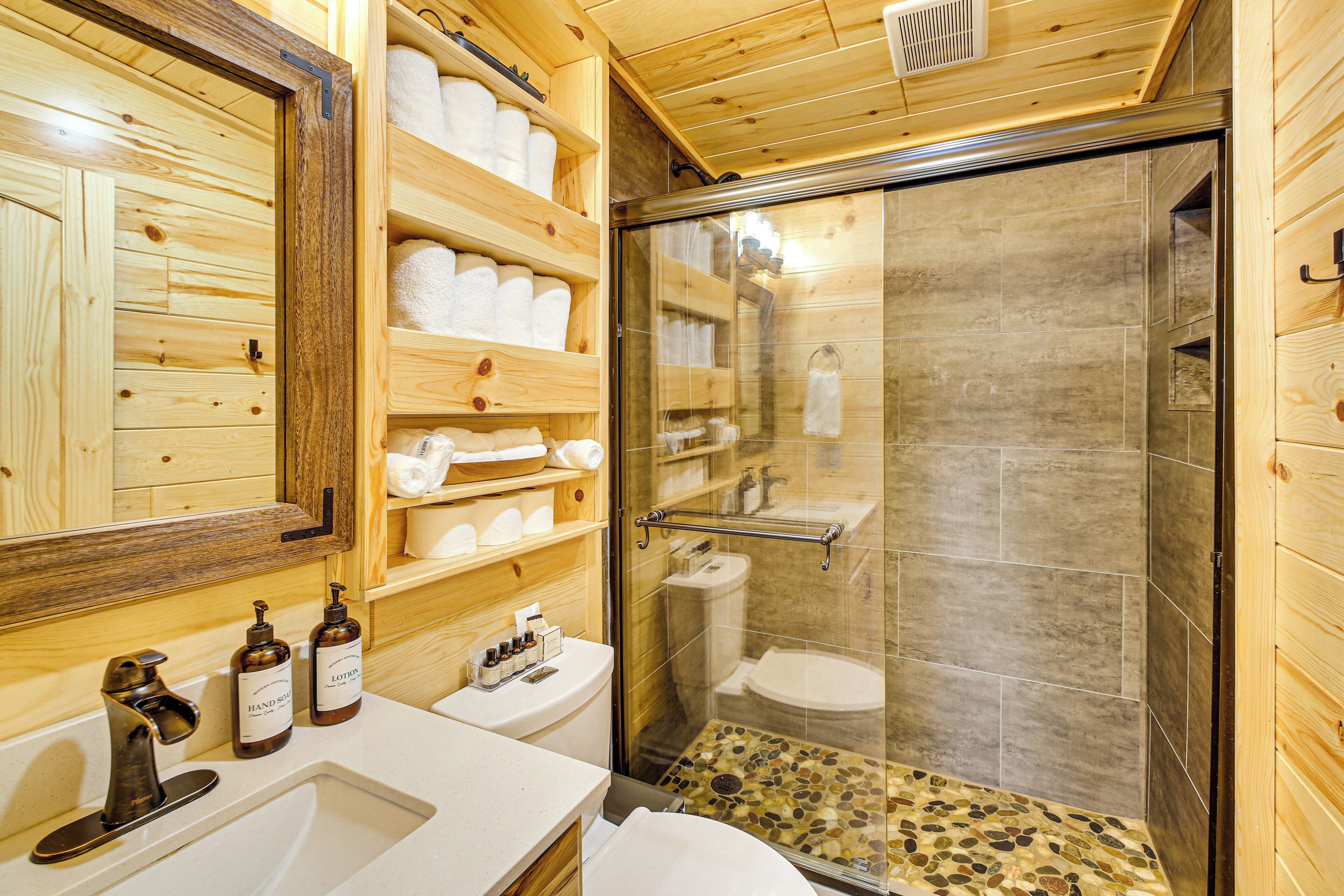 Un baño de madera con cabina de ducha de vidrio, un lavabo y estantes con toallas.