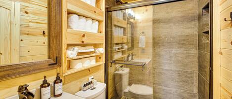 Un baño de madera con cabina de ducha de vidrio, un lavabo y estantes con toallas.
