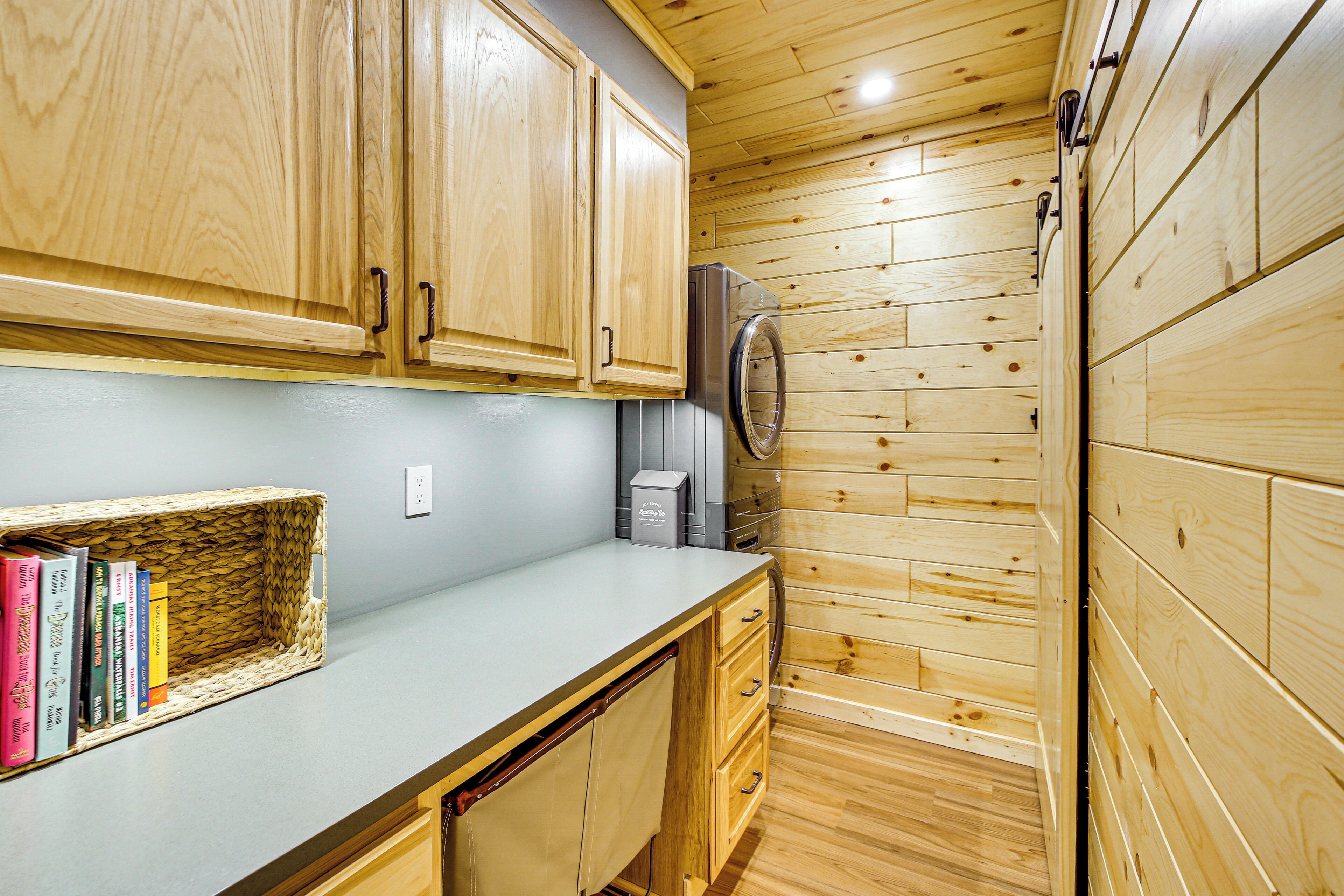Cocina compacta con armarios de madera, lavadora integrada y una encimera con una cesta de libros.