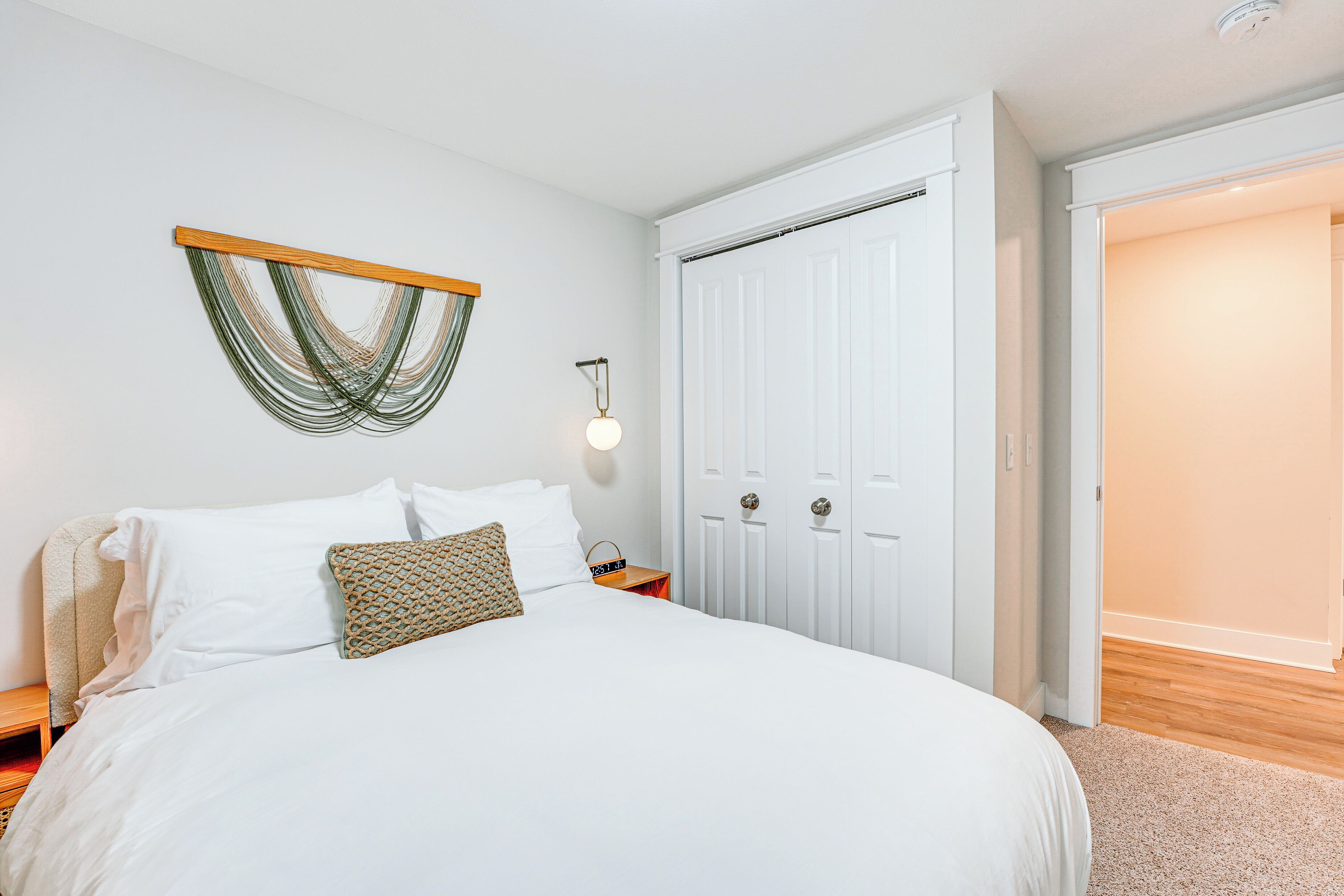 A neatly made bed with white linens and a patterned pillow, a bedside table with a lamp, and a wooden headboard.