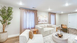 A modern living room with a large potted plant, a beige sofa set, a round coffee table, and a painting on the wall.