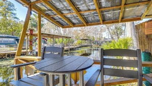A covered outdoor seating area with a table and chairs, overlooking a water body with docks and boats. - < 1 Mi to Boat Ramp: Canal-front Retreat in Astor! (Astor)
