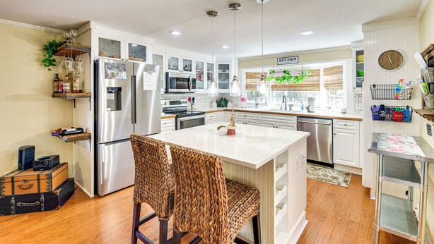 A modern kitchen with white cabinetry, stainless steel appliances, and a central island with bar stools. - < 1 Mi to Boat Ramp: Canal-front Retreat in Astor! (Astor)