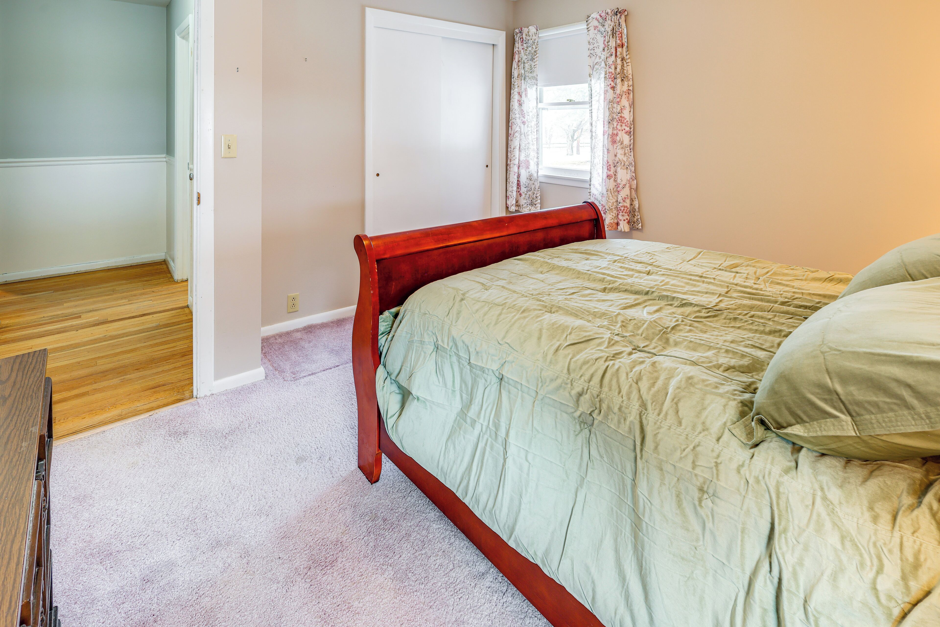 Quarto com estrutura de cama de madeira, colcha verde e tapete em tons claros.