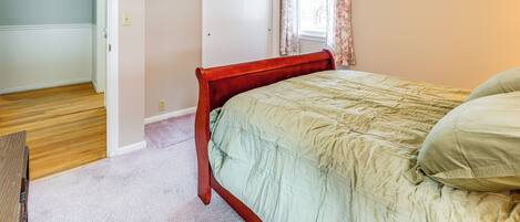 A bedroom with a wooden bed frame, a green bedspread, and a light-colored carpet.