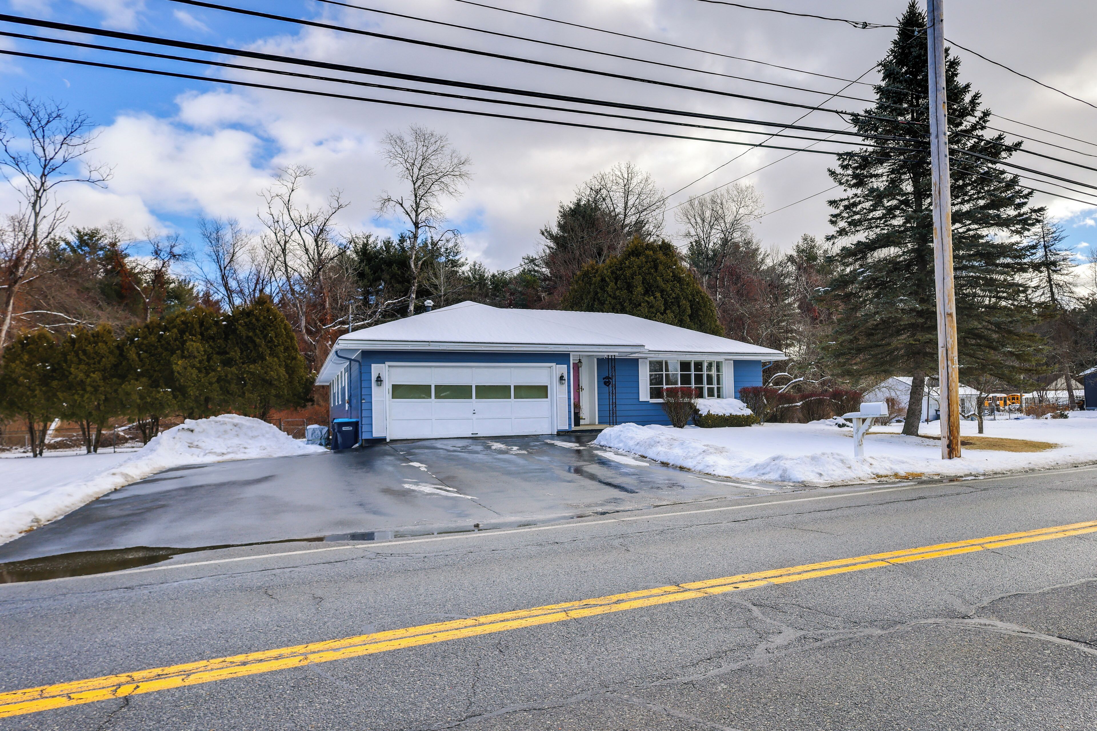 Une maison à deux étages avec un garage, entourée d’un paysage enneigé et d’arbres.
