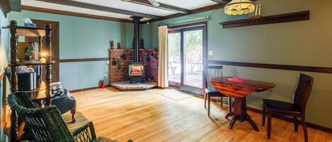 A room with a wooden floor, a fireplace, a dining table with chairs, a ceiling fan, and a window with curtains.