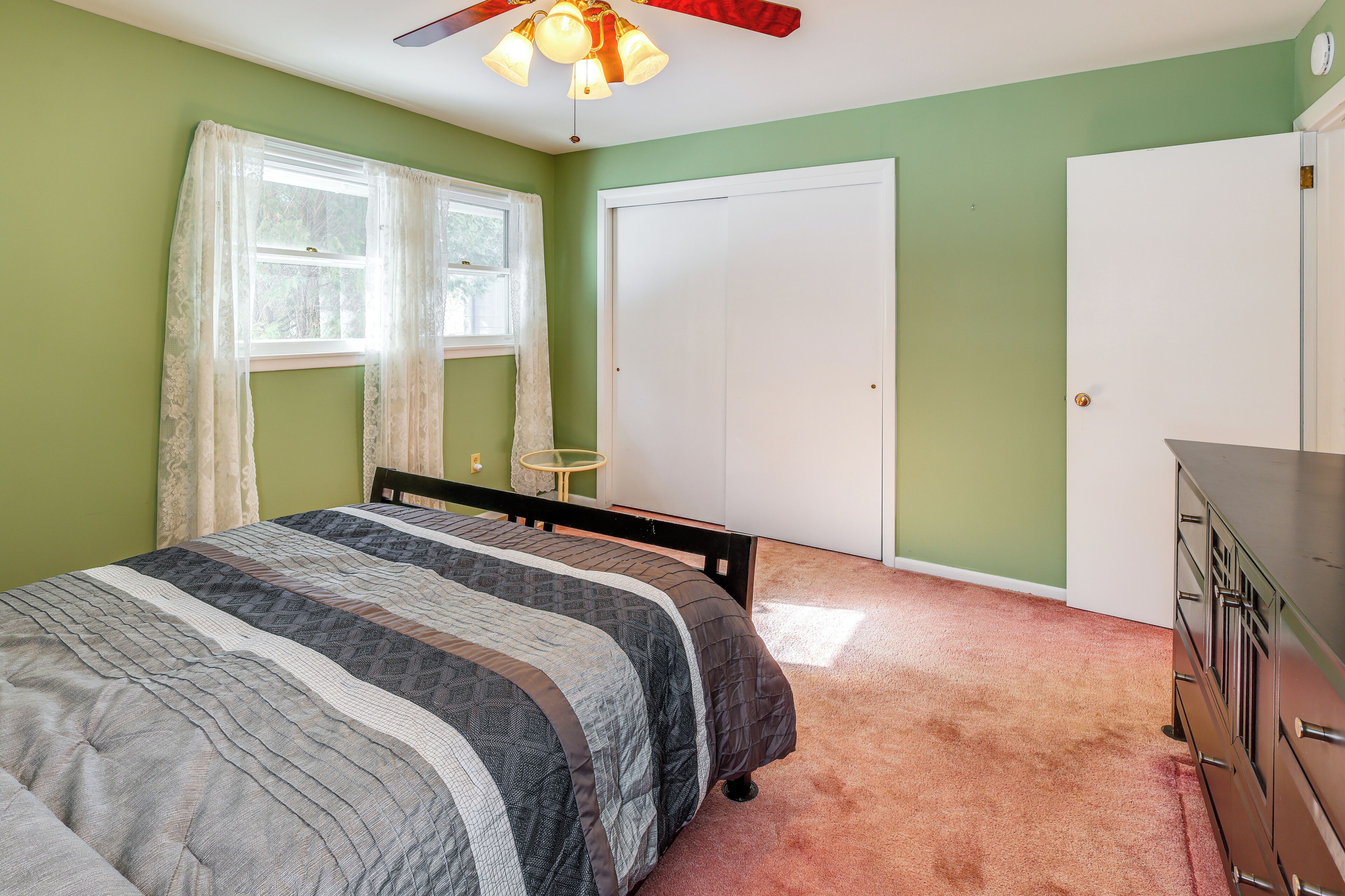 A bedroom with a bed, a dresser, a ceiling fan, and a window with curtains.