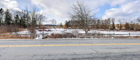 A paved road with a yellow dividing line, a wooden fence, and leafless trees in a rural setting.