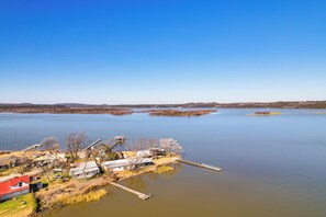 A lakeside property with a dock, several buildings, and a clear view of the surrounding water and distant hills. - Dock & Patio: Possum Kingdom Lake House (Graford)