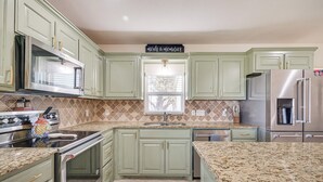 A kitchen with green cabinets, a granite countertop, stainless steel appliances, and a window with a view. - Dock & Patio: Possum Kingdom Lake House (Graford)