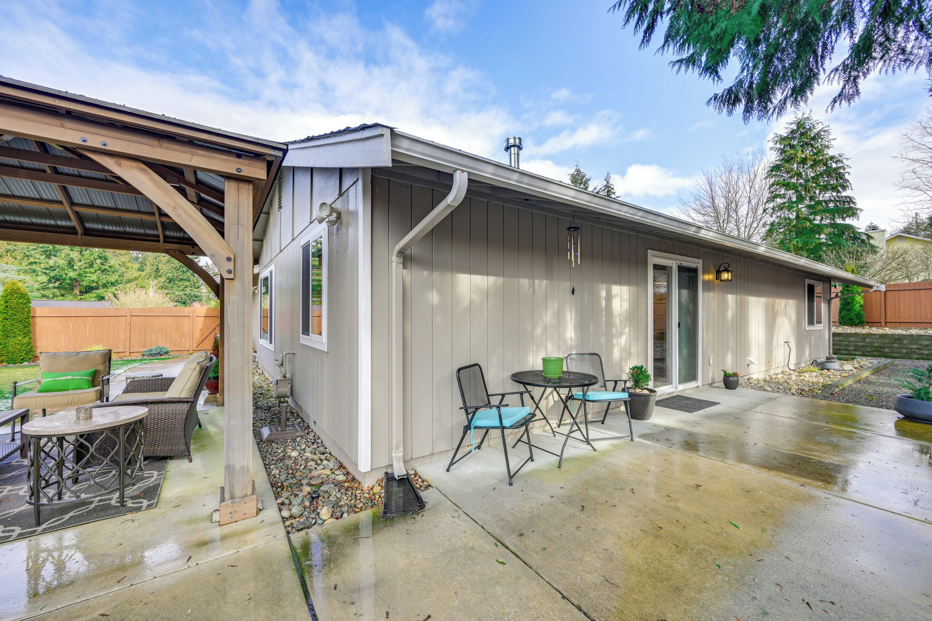 Un patio techado con mobiliario exterior, piso de concreto y estructura de pérgola de madera.