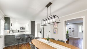Una cucina moderna con mobili bianchi, un'isola centrale e un'area pranzo con tavolo e sedie in legno.