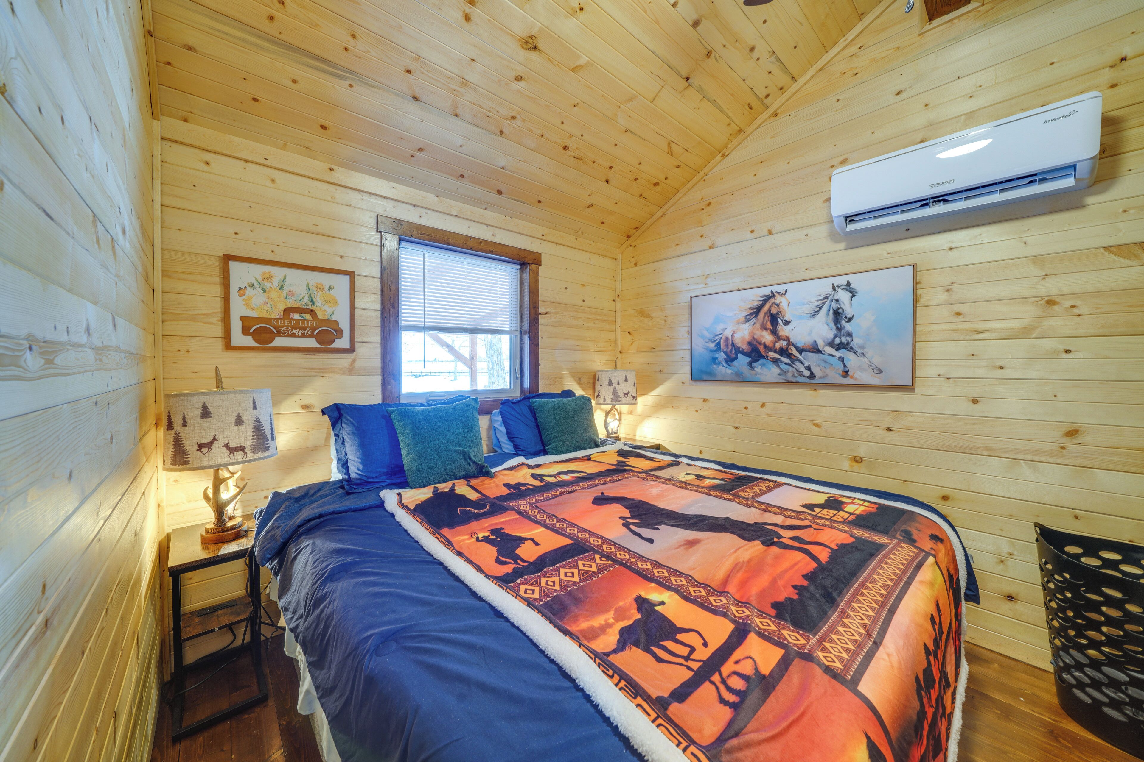 Un dormitorio de cabaña de madera con cama, dos mesitas de noche, una ventana y un aire acondicionado de pared.