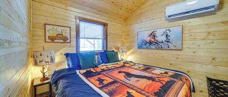 Un dormitorio de cabaña de madera con cama, dos mesitas de noche, una ventana y un aire acondicionado de pared.
