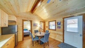 L’intérieur d’un chalet en bois, avec une table à manger, des chaises, un réfrigérateur et un lit à l’arrière-plan.