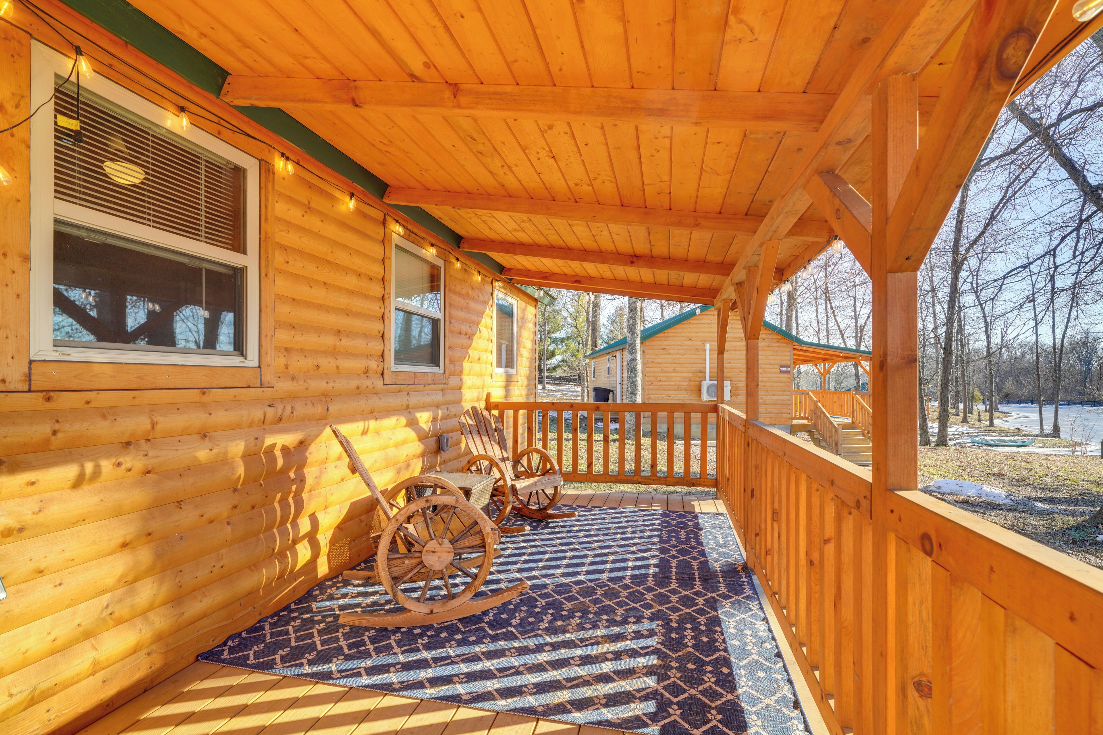 A log cabin with a porch, wooden wheelchairs, and a patterned rug.