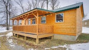 A wooden cabin with a porch and string lights, surrounded by snow and trees. - La Grange Cabin on a Racehorse Farm w/ Pond Views! (La Grange)
