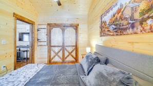 A wooden cabin bedroom with a bed, a ceiling fan, and a painting of a landscape on the wall. - La Grange Cabin on a Racehorse Farm w/ Pond Views! (La Grange)